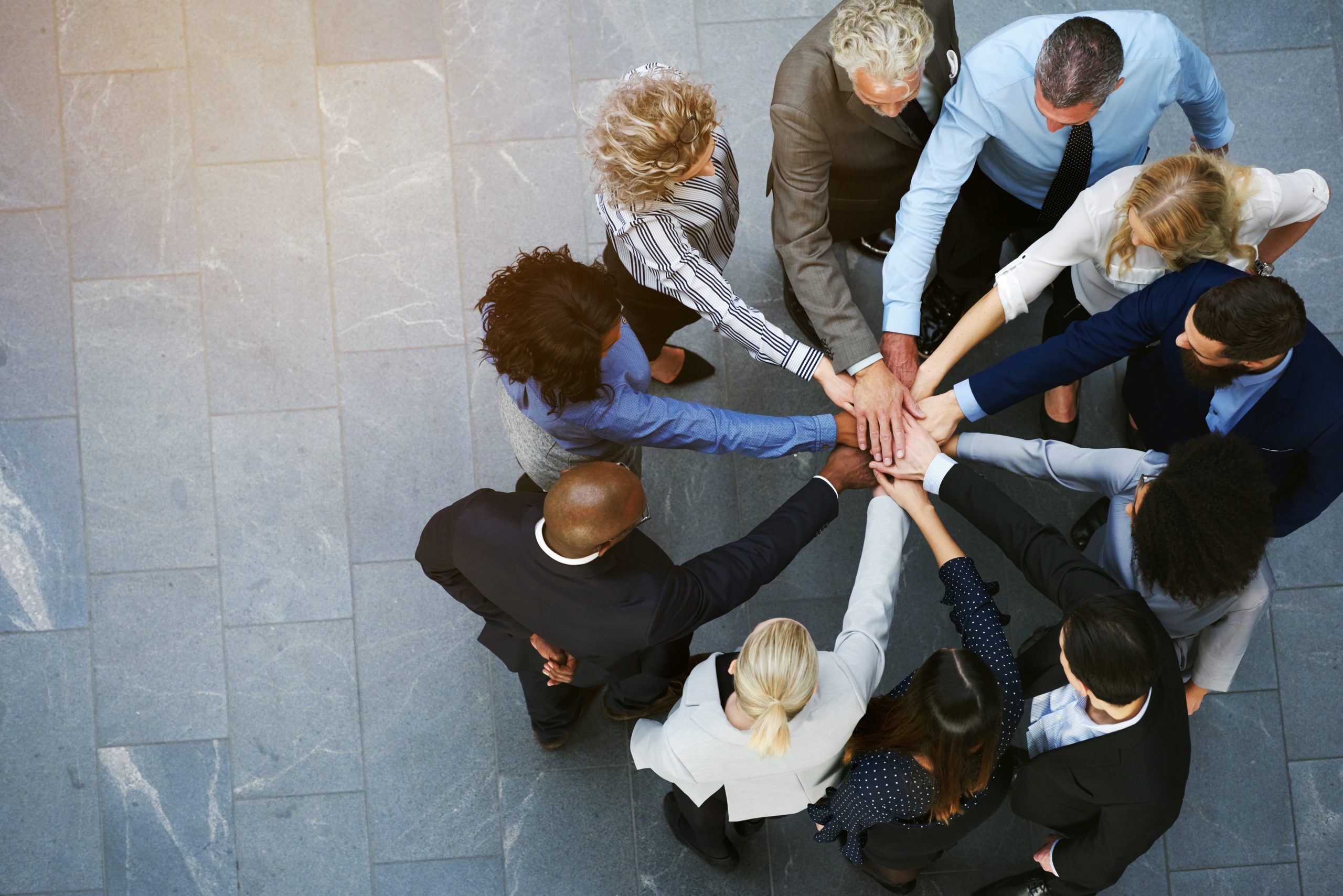 High angle view of a team of united coworkers standing with their hands together in a huddle in the lobby of a modern office building